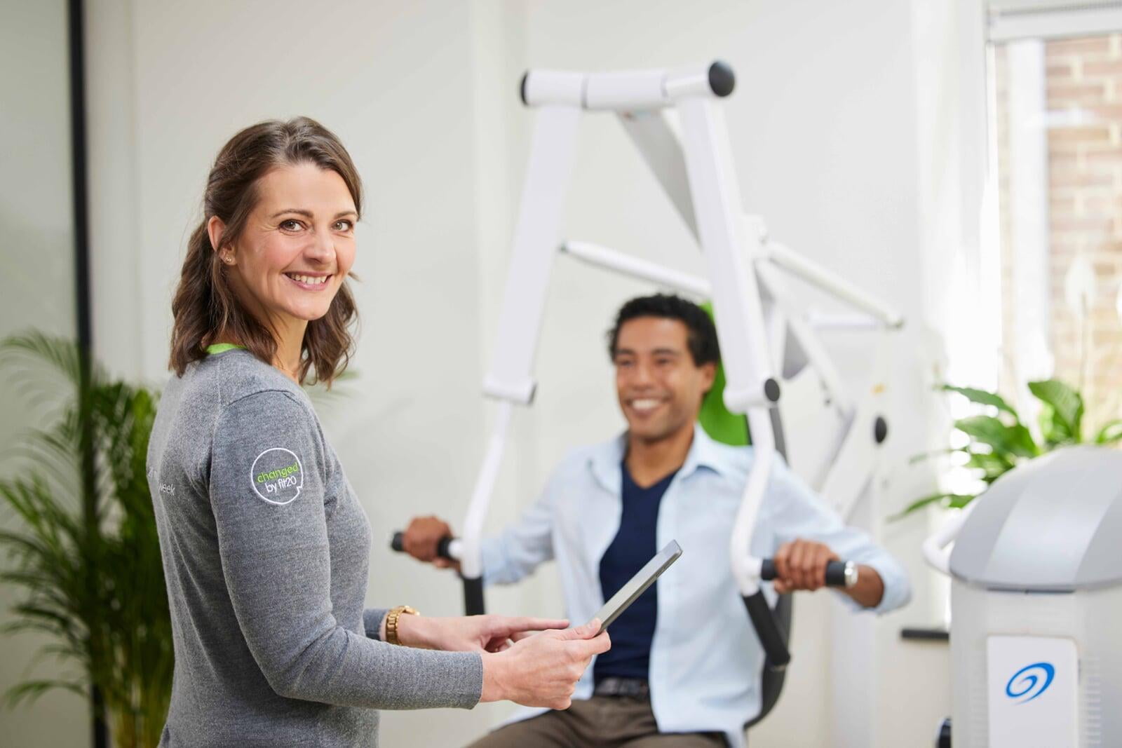 Kvinnlig Fit20-tränare med tablet följer kundens pass i en ljus studio